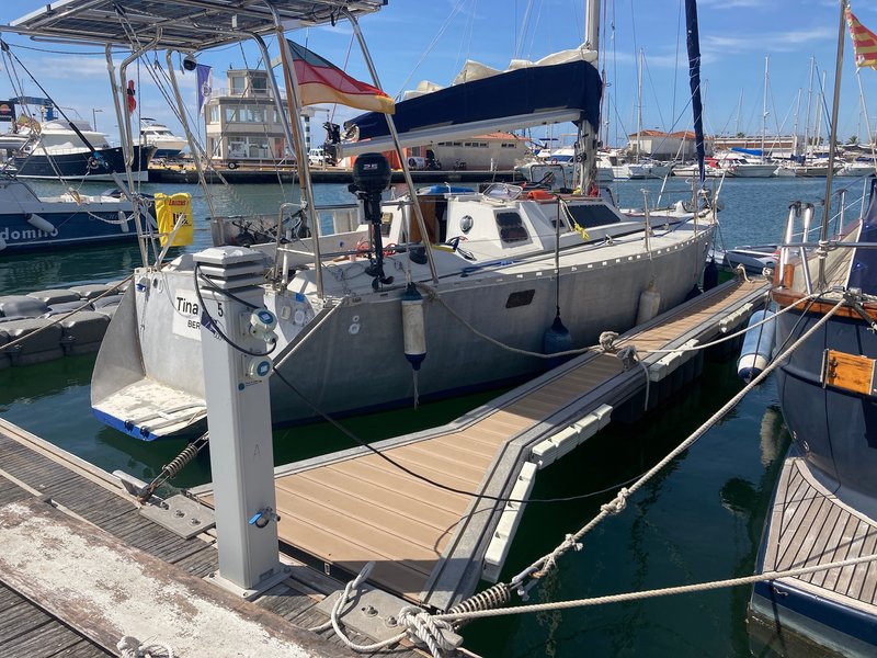Tinarasia moored stern-to at a marina pontoon, with her name and homeport painted on the transom and other yachts in the background