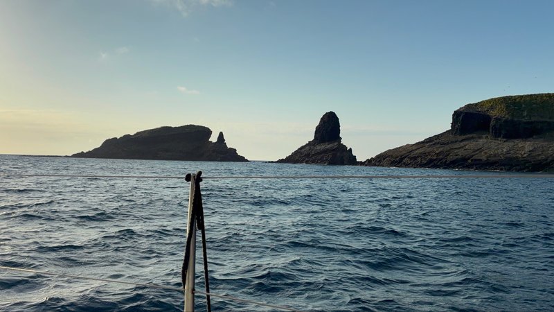 Jagged volcanic rock islets rising from the sea at dawn, seen past the boat's bow pulpit