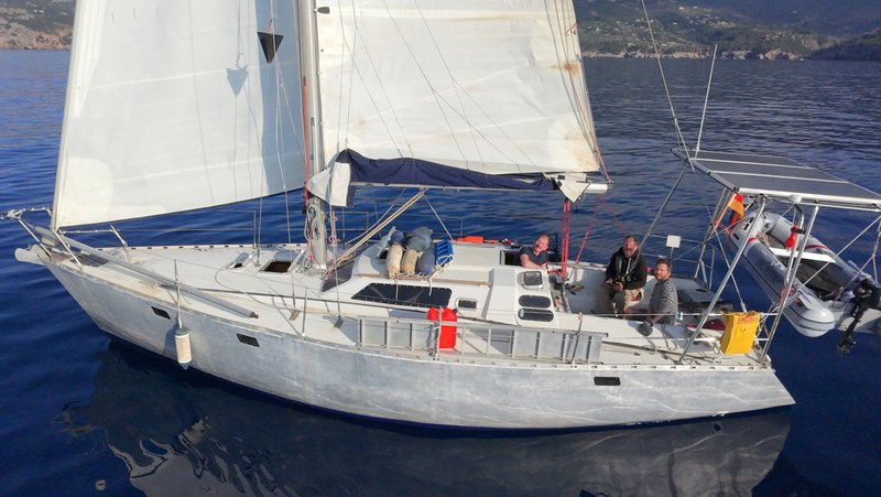 Aerial view looking down onto Tinarasia's deck under sail, showing three crew in the cockpit and the solar arch over the stern