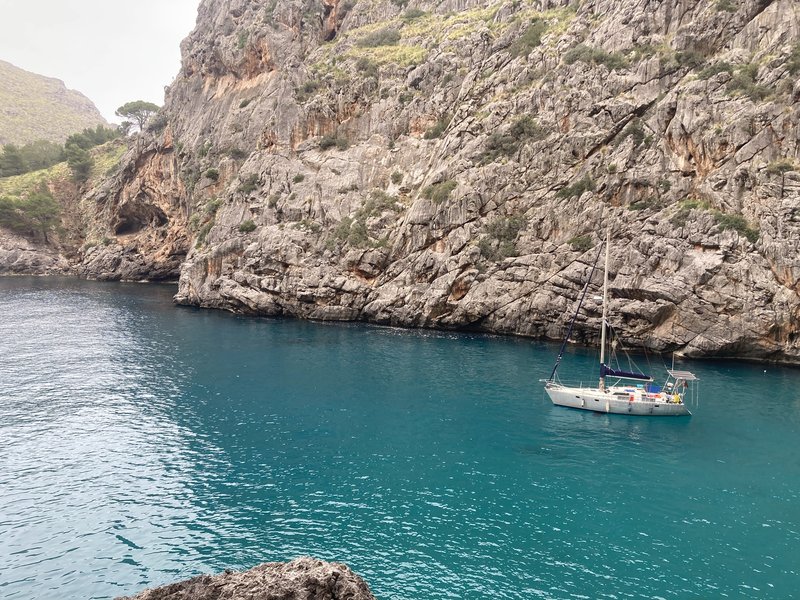 Tinarasia at anchor in a narrow, steep-walled rocky cove with turquoise water